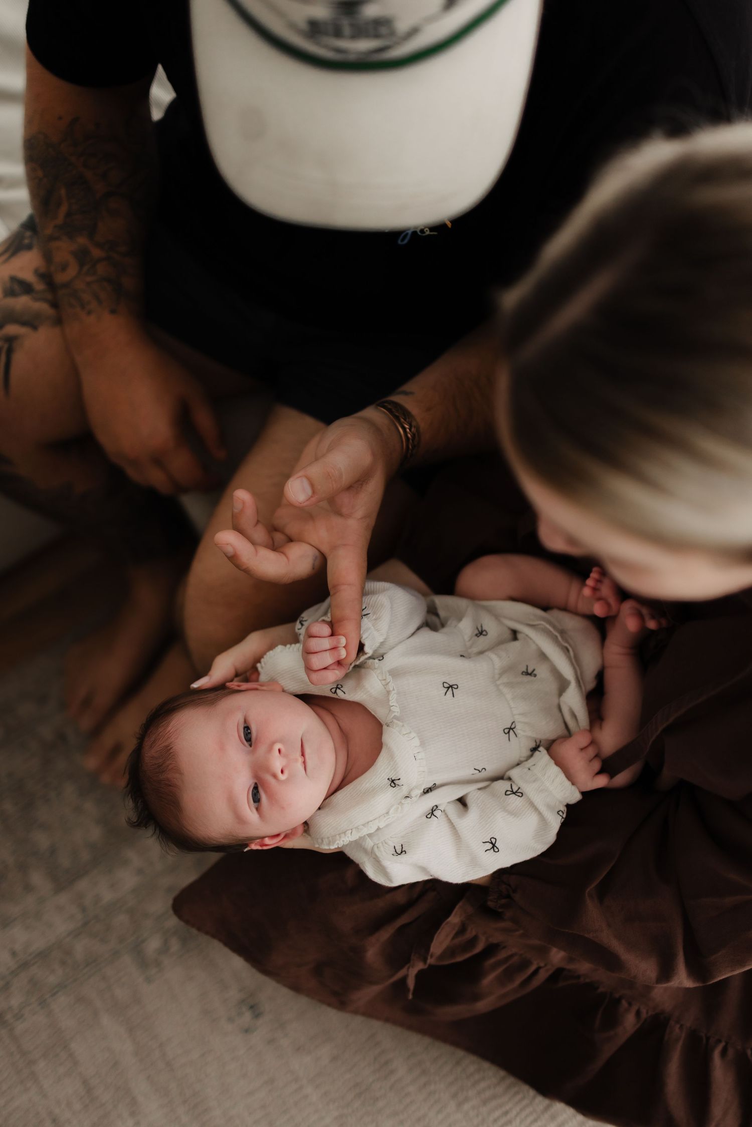 A baby in white onesie lies on brown fabric while gentle hands provide comfort.