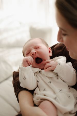 A tender moment shows a sleeping newborn being cradled in soft white clothing.