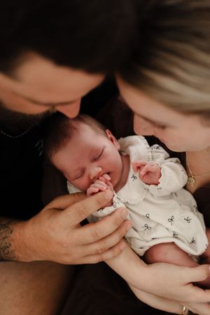 Intimate black and white portrait showing gentle parental affection with a newborn baby in white clothing.