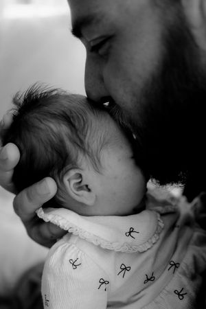 A tender black and white photo series showing a parent kissing a baby wearing a patterned bib.