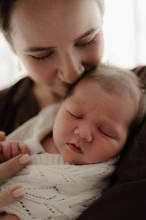 A tender moment captured in soft lighting as someone kisses a sleeping baby's forehead.