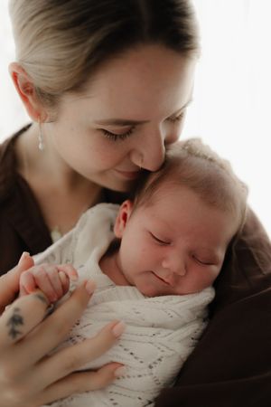 Tender moment between parent and sleeping newborn wrapped in white lace.