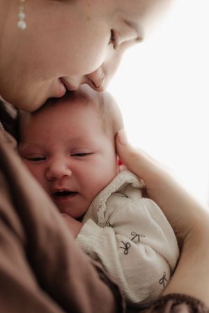 A tender close-up moment between parent and newborn baby in soft lighting.