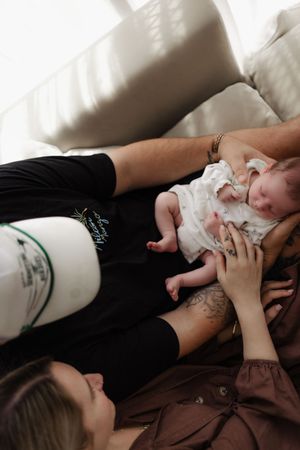 A tender moment on a couch showing a newborn baby in white clothing being held while resting on soft pillows.