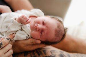 A peaceful sleeping baby rests against a caregiver in a white onesie.