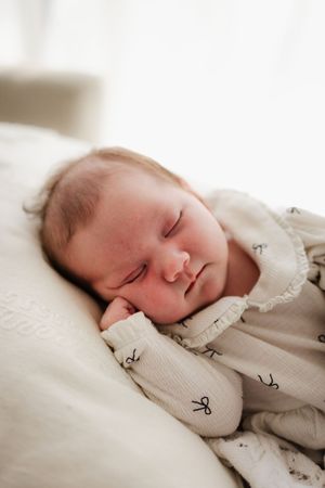 Sleeping newborn in white patterned outfit rests on soft white bedding.