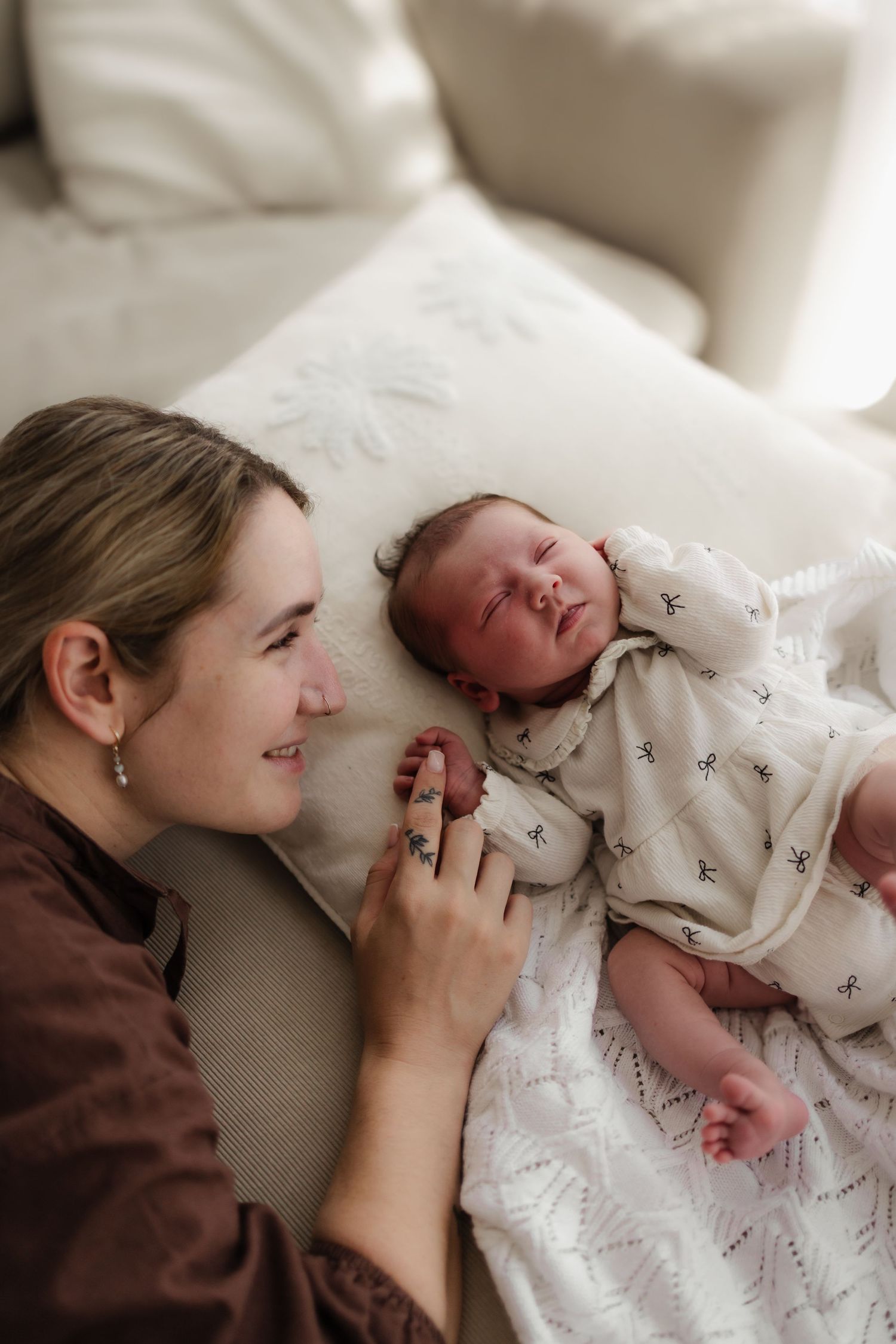 A peaceful scene of a sleeping newborn in white clothing resting on plush white cushions beside someone in brown.