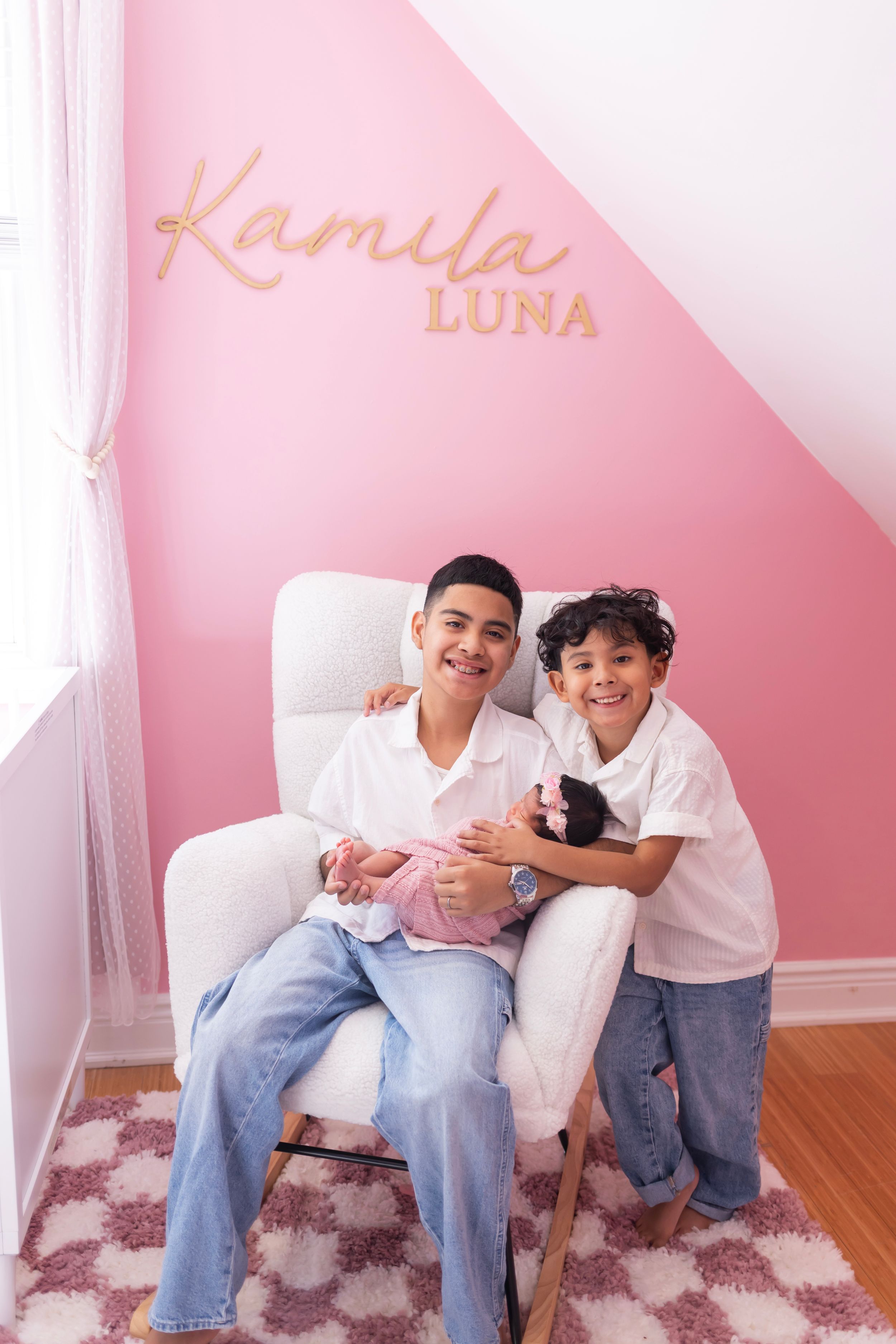 Two people in white shirts and jeans sit together on a pink carpet against a pink wall with decorative text.