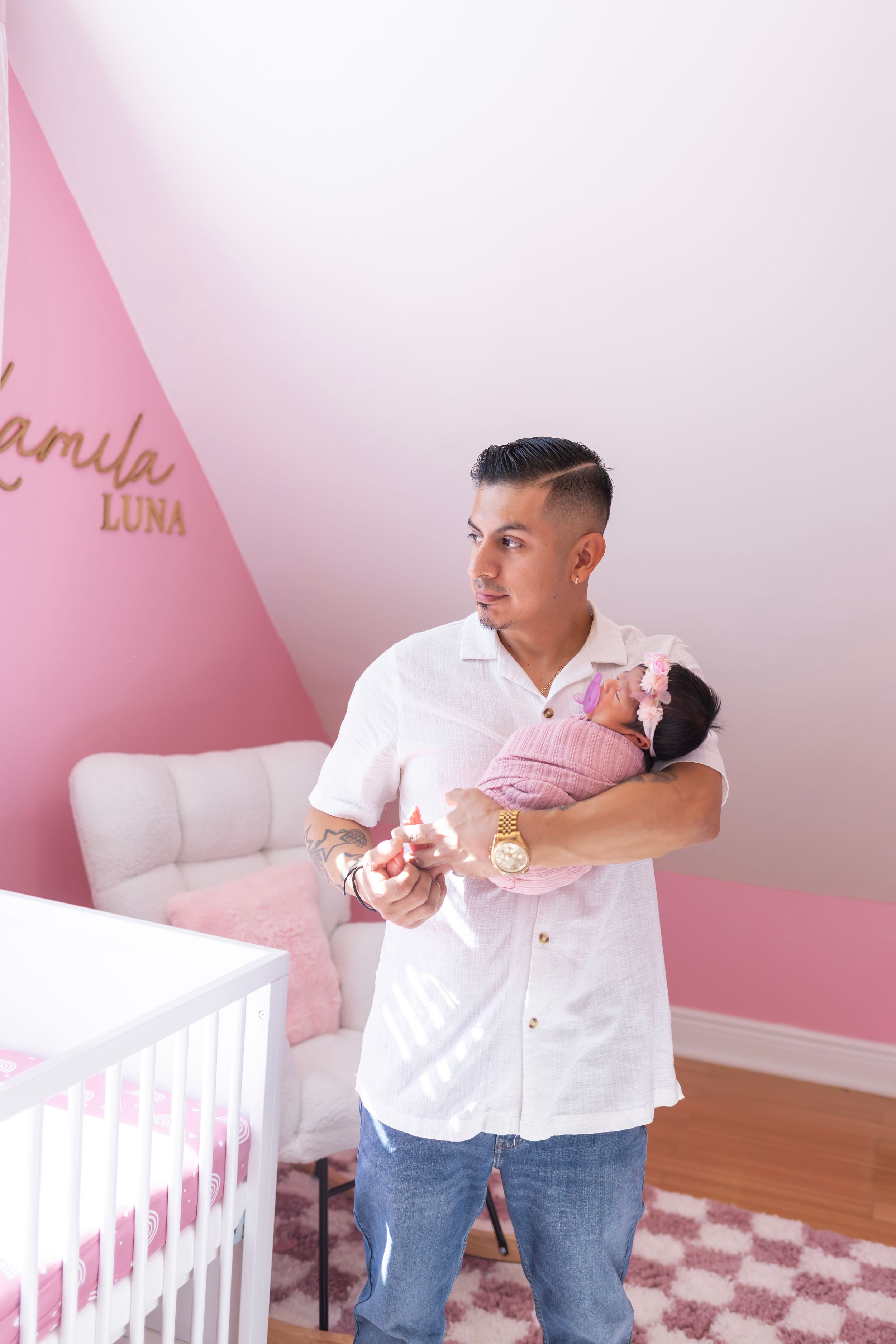 Parents dance together in a pink nursery room with white crib and geometric wall design.