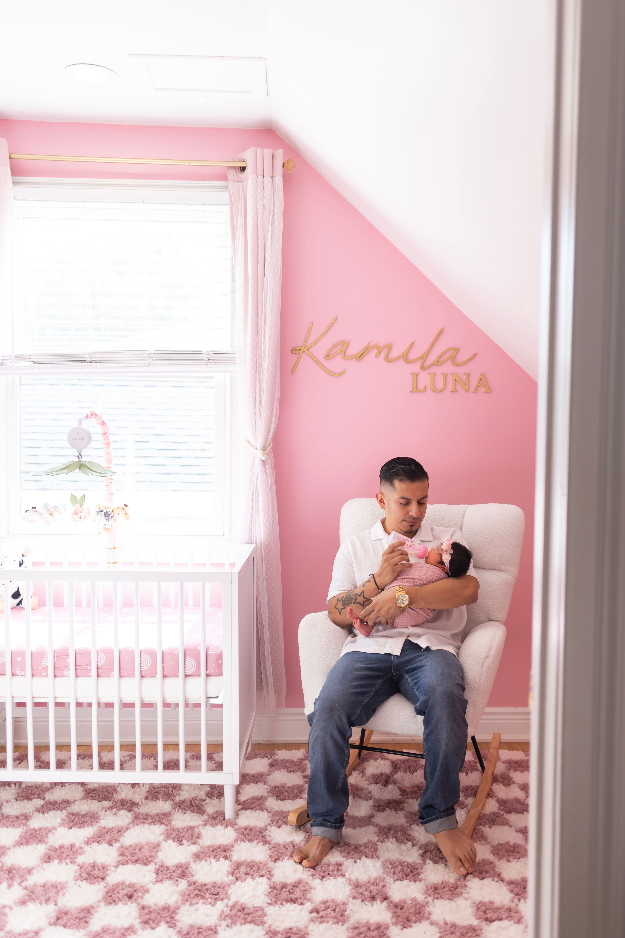 Parent and newborn share tender moments in pink nursery with white crib and elephant-patterned rug.