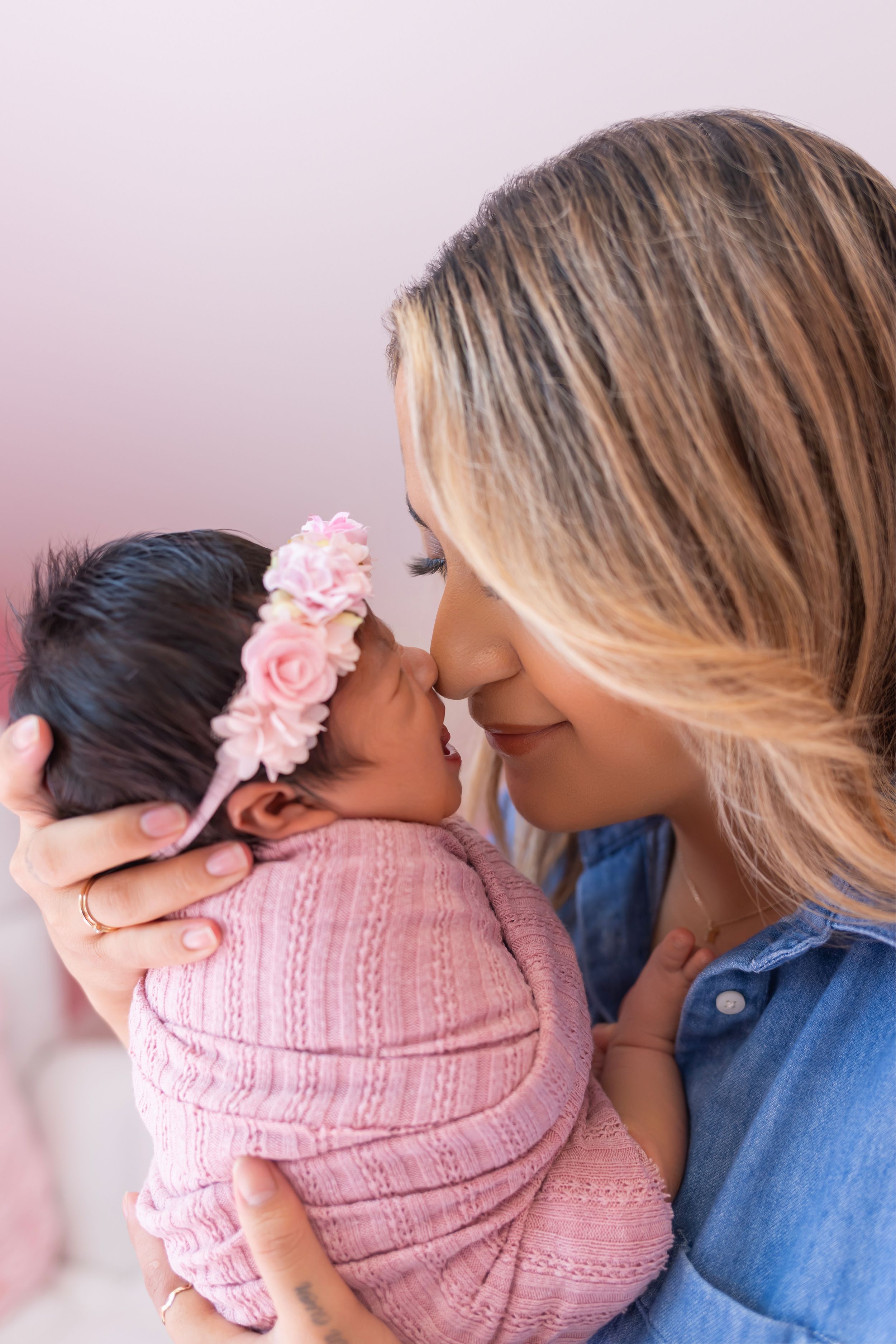 A series of tender moments showing a parent in denim cradling a baby wearing a pink knit outfit and floral headband.