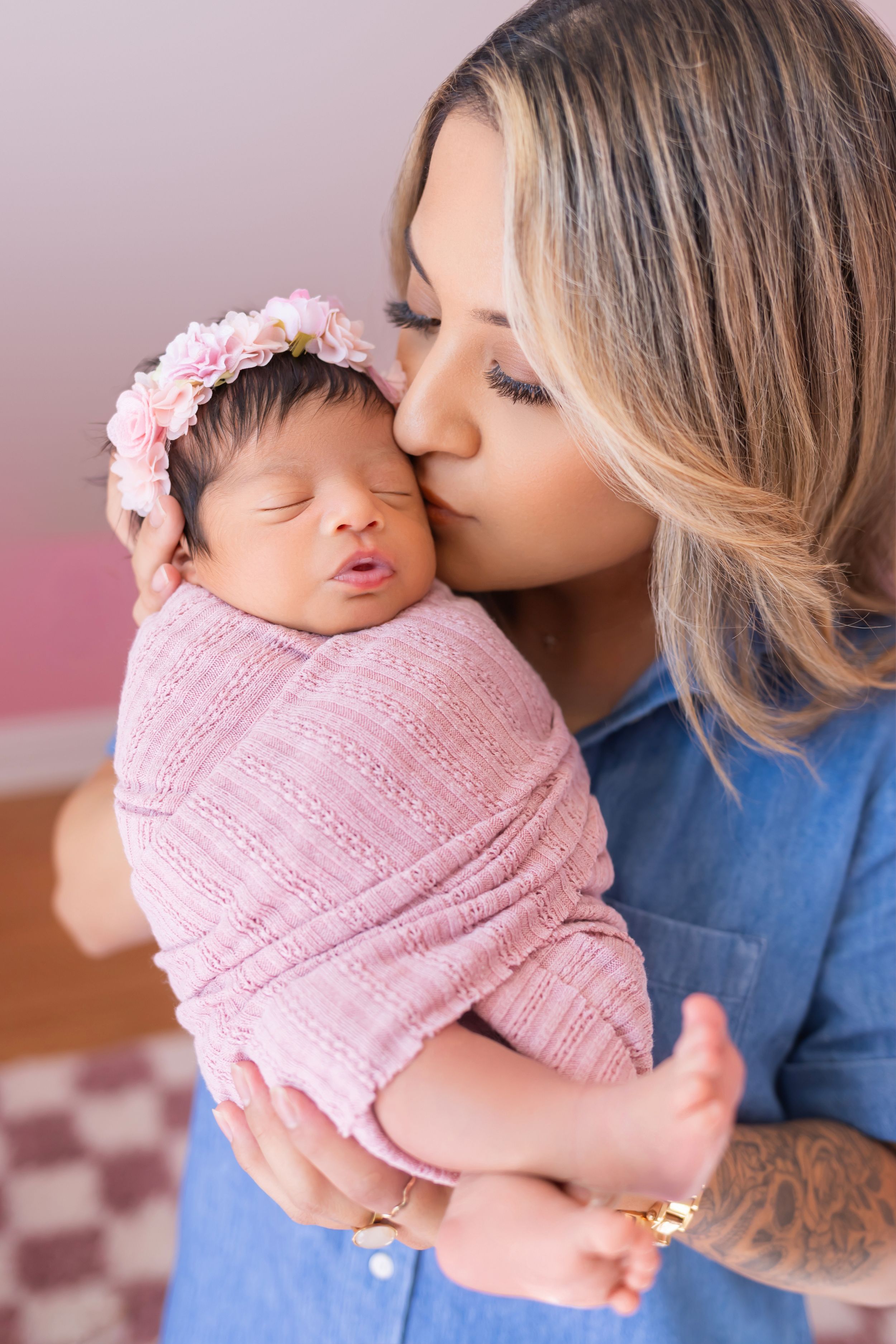 A tender moment captured between parent and newborn baby wrapped in soft pink knit blanket.