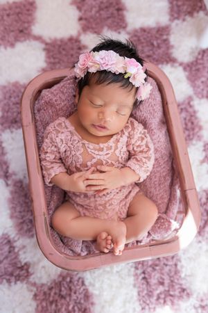 Newborn baby sleeping peacefully in pink dress on mauve bed with floral headband in professional photo collage.