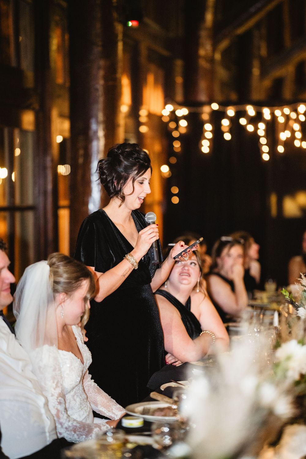 Wedding guests enjoy an intimate candlelit reception dinner under twinkling string lights in a rustic venue.