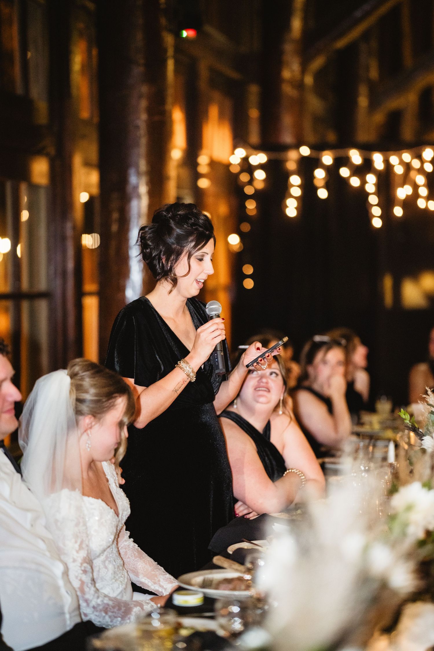 Wedding guests enjoy an intimate candlelit reception dinner under twinkling string lights in a rustic venue.