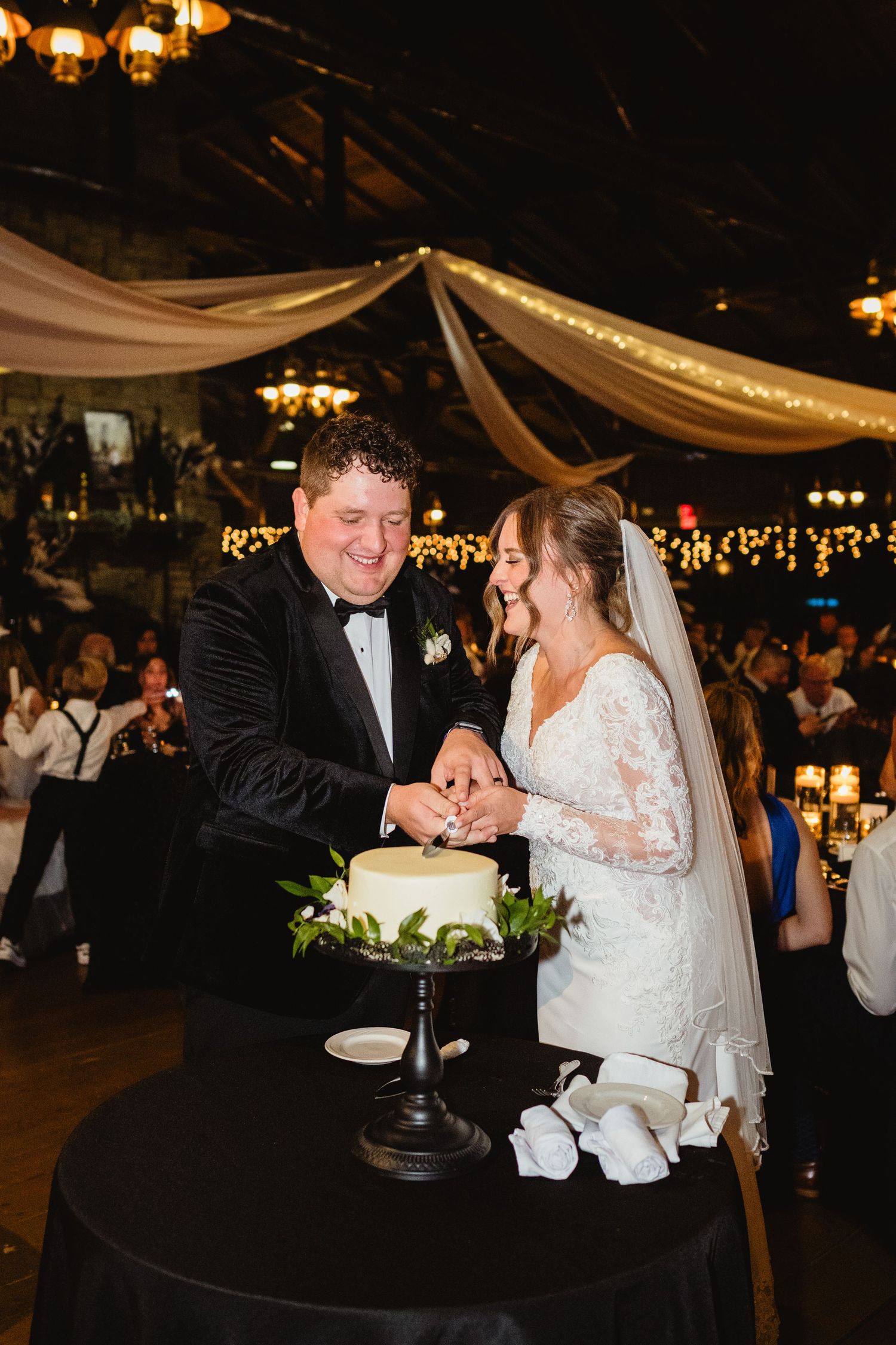 Newlyweds share a joyful moment while cutting their elegant black and white wedding cake at an indoor reception.
