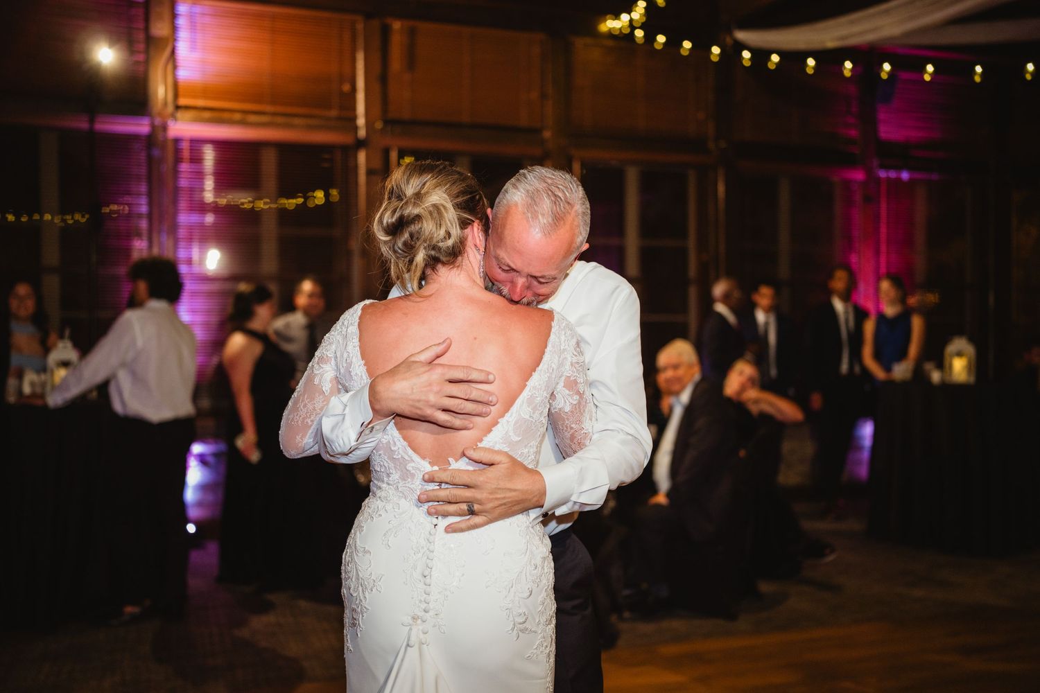 Newlyweds share a romantic dance together under string lights at their evening wedding reception.