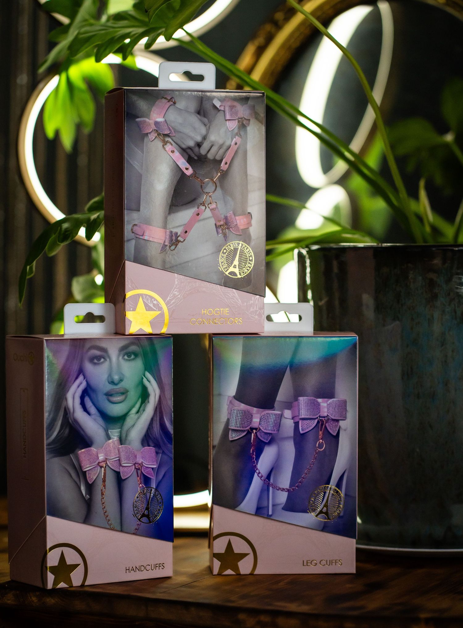 Three boxes of decorative leg accessories with bow designs displayed against plant background.