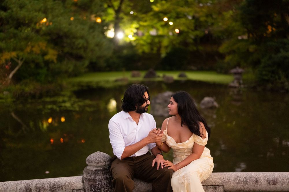 Couple sitting together by a reflective pond at dusk, holding hands in a lush garden.