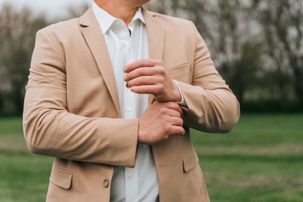Close-up view of a person wearing a beige blazer and white dress shirt adjusting their sleeve cuff.