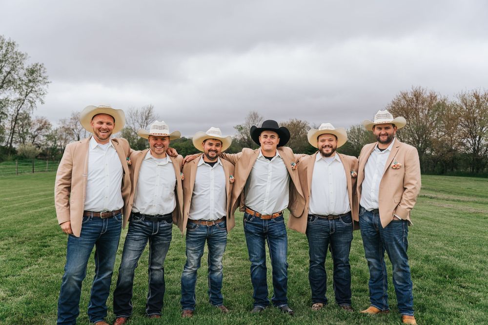 A group wearing blue jeans and casual attire stands together in a green field on an overcast day.