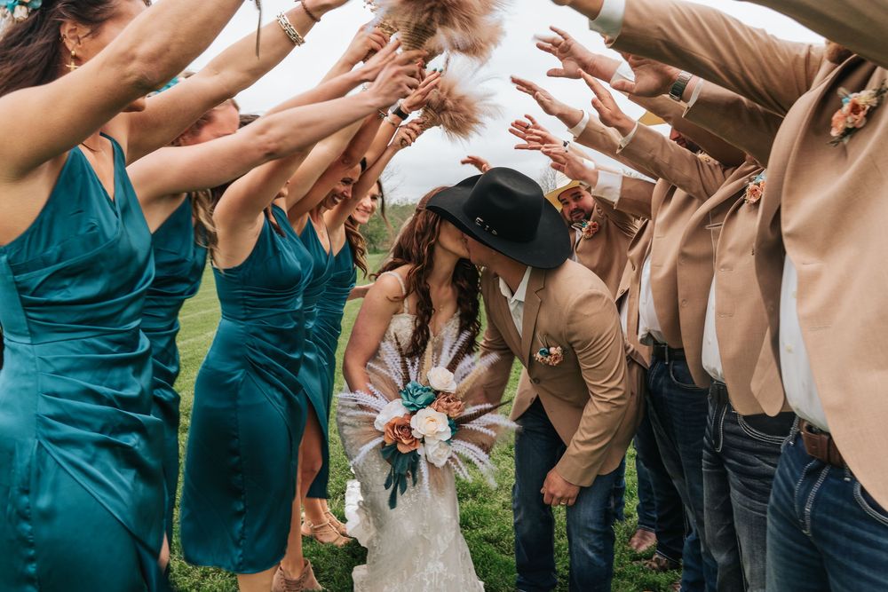 Wedding guests form a tunnel with raised arms for the newlyweds to walk through during an outdoor celebration.
