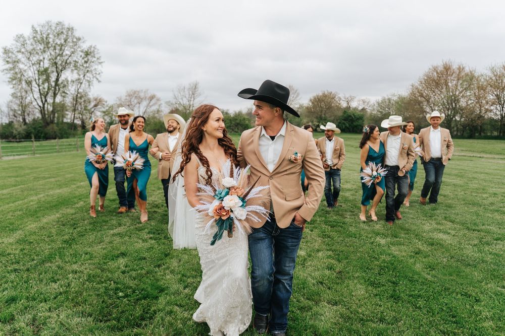 Joyful couple dances together in a green field during a rustic outdoor wedding celebration.