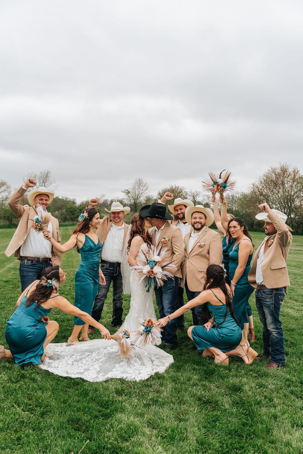 Wedding party celebrates with fun poses and laughter in a green field on an overcast day.