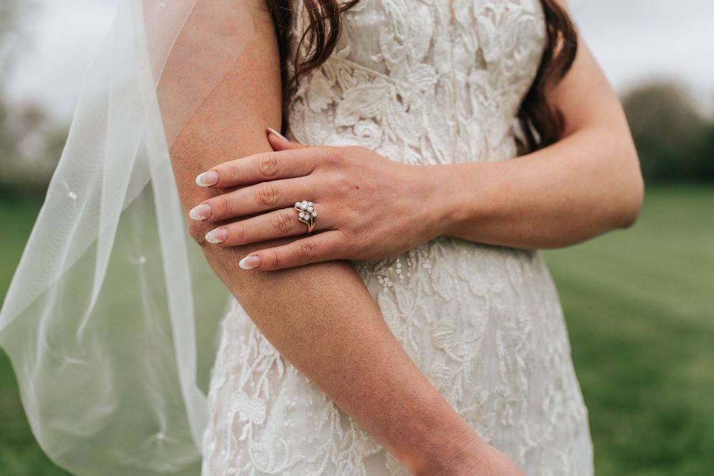 Delicate details of a lace wedding dress sleeve with floral embroidery against a soft outdoor background.