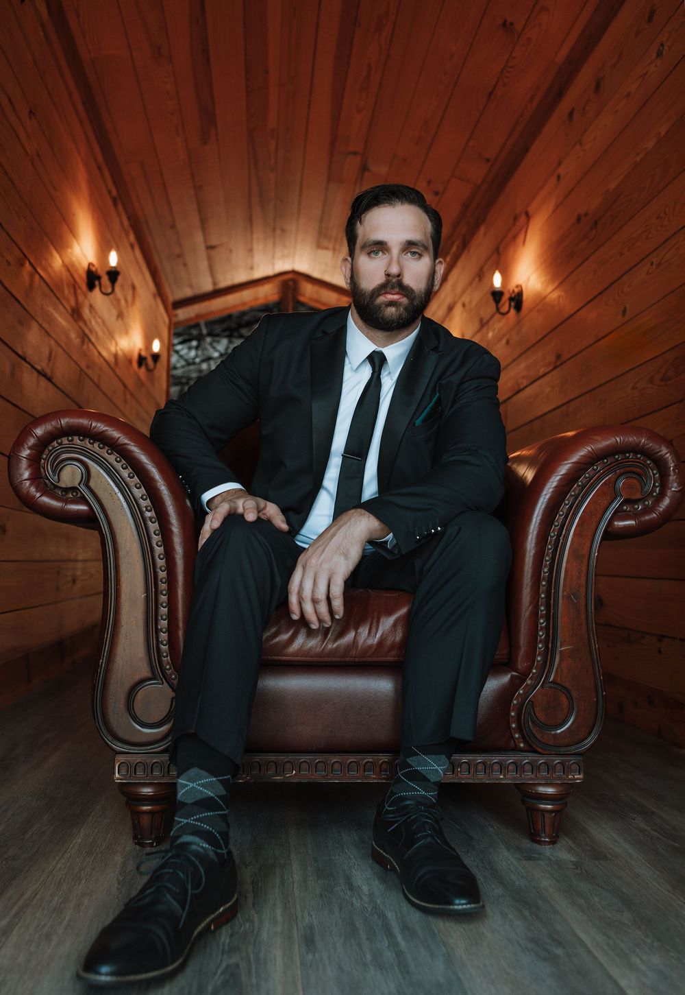 A series of moody photos showing a person in a black suit seated on a brown leather chesterfield couch in a wood-paneled room.