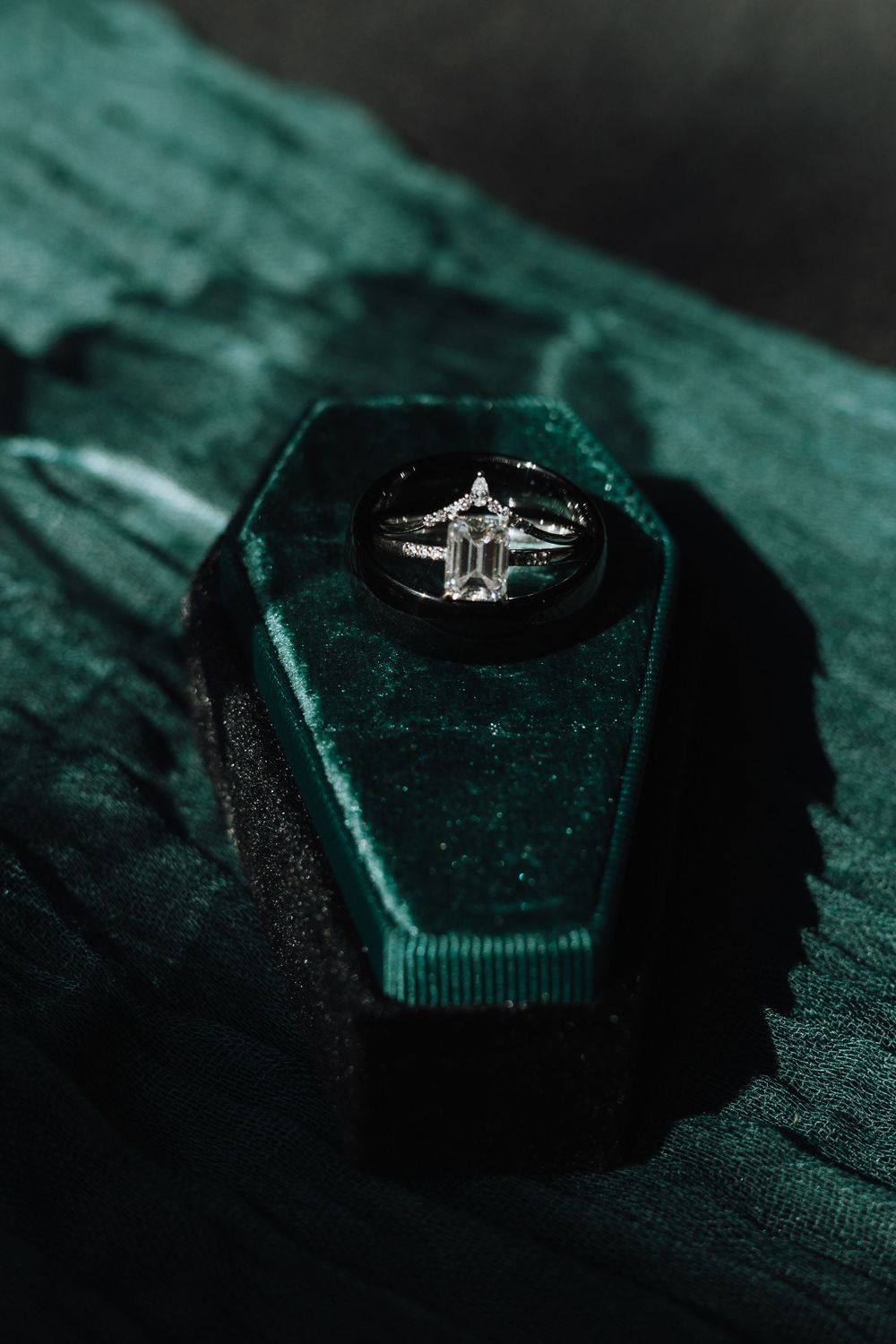 Diamond engagement ring displayed in a dark green velvet hexagonal ring box with moody lighting.