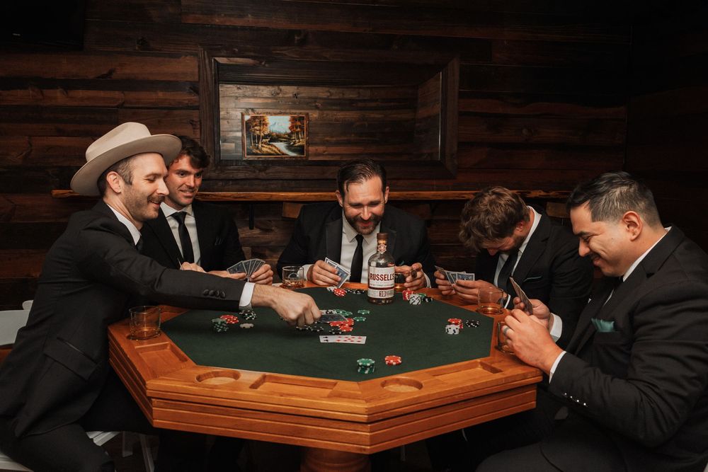 People playing poker at a wooden gaming table in a dimly lit room.