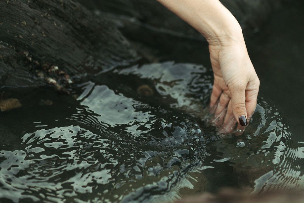 Hand dips into dark rippling water creating concentric circles and reflective patterns on the surface.