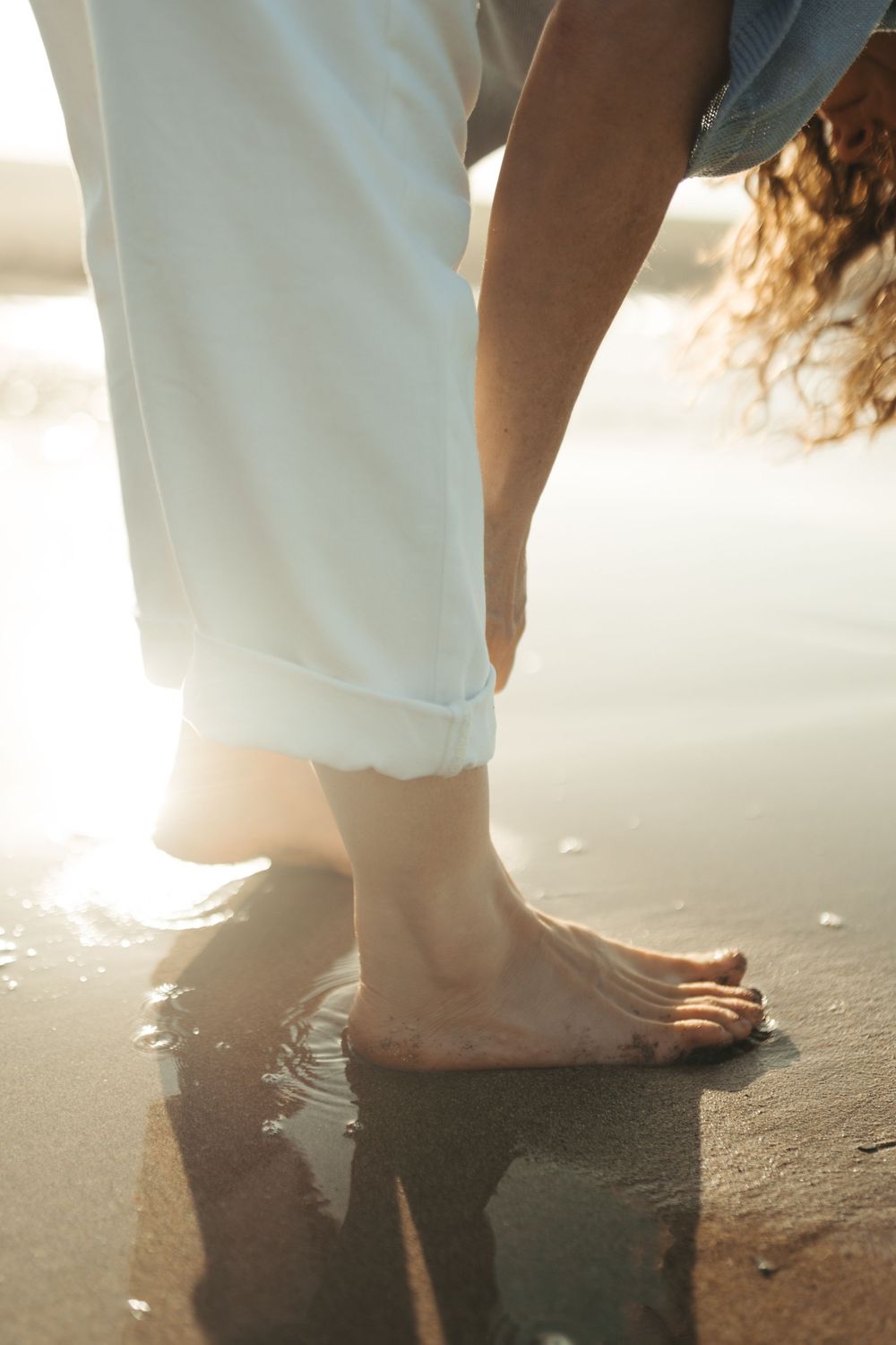 Bare feet walking on wet sand at the beach during sunset with gentle waves washing over them.