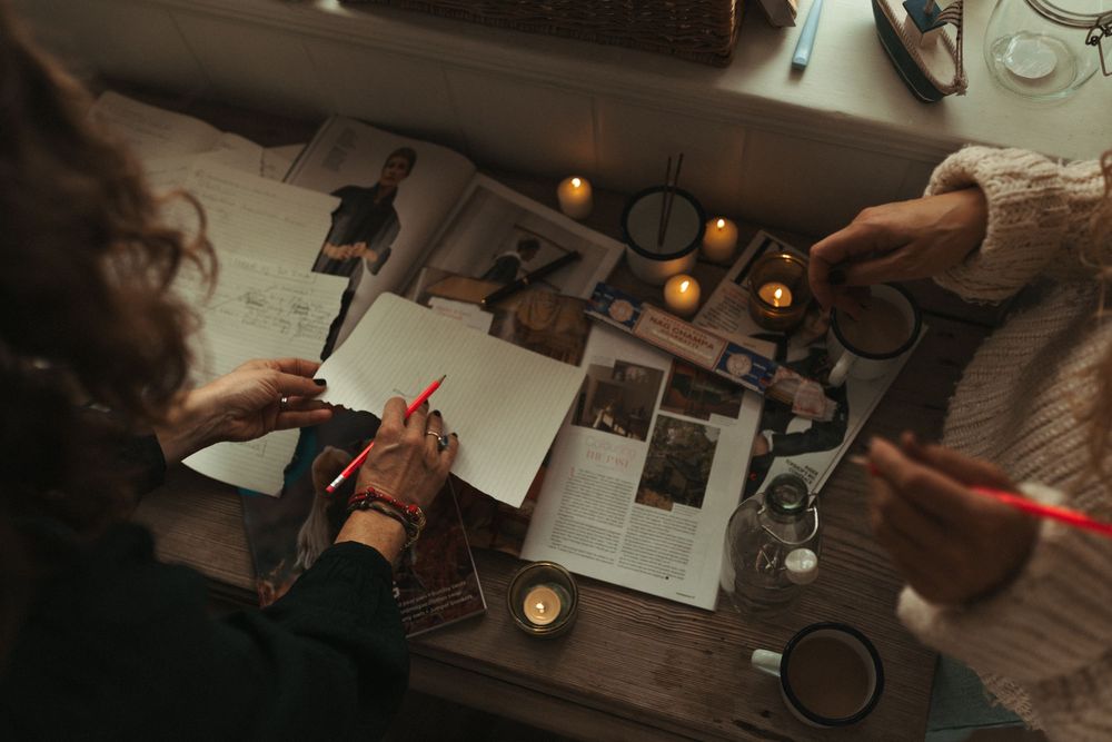 Overhead view of hands writing and working at a rustic wooden desk with candles and oranges.