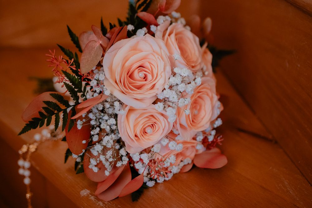Peach roses and baby's breath arranged in a romantic wedding bouquet on wooden surface.