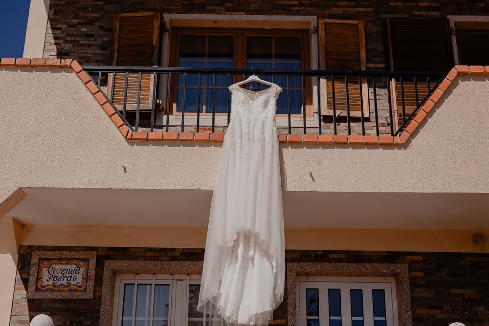 White wedding dress hanging outside against a rustic building facade.