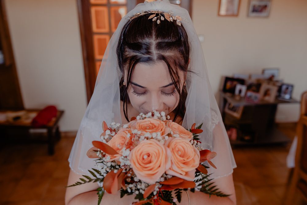 A bride holding a bouquet of peach roses poses for a portrait.