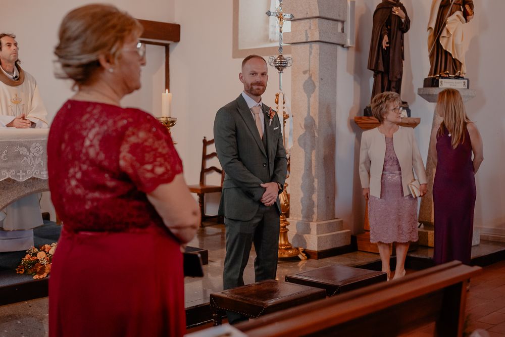 Wedding ceremony scene in a church with guests in red and green attire.