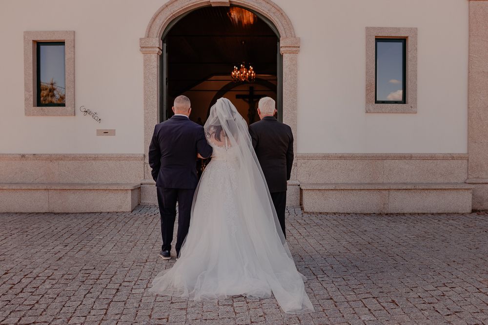 Bride in white gown walking into church entrance with two people in dark suits.