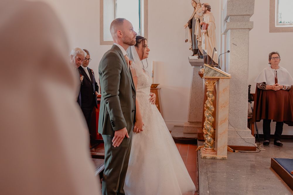 Bride and groom standing at church altar during wedding ceremony, with guests seated nearby.
