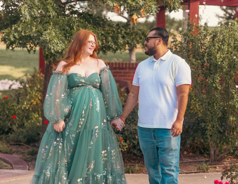 A couple stands together outdoors under trees wearing coordinated outfits of teal and white.
