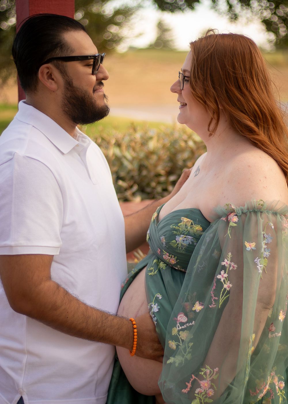 A couple shares an intimate moment outdoors, with the person in a floral sage green dress and another in a white shirt.