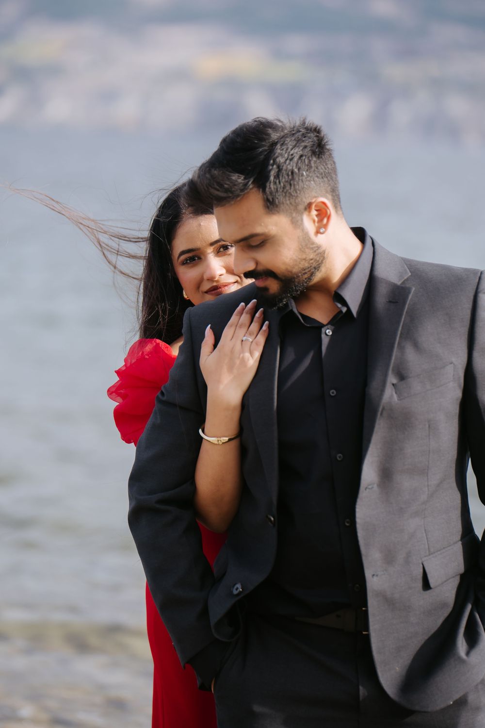 A couple in formal attire share an intimate moment while laughing together by the water.