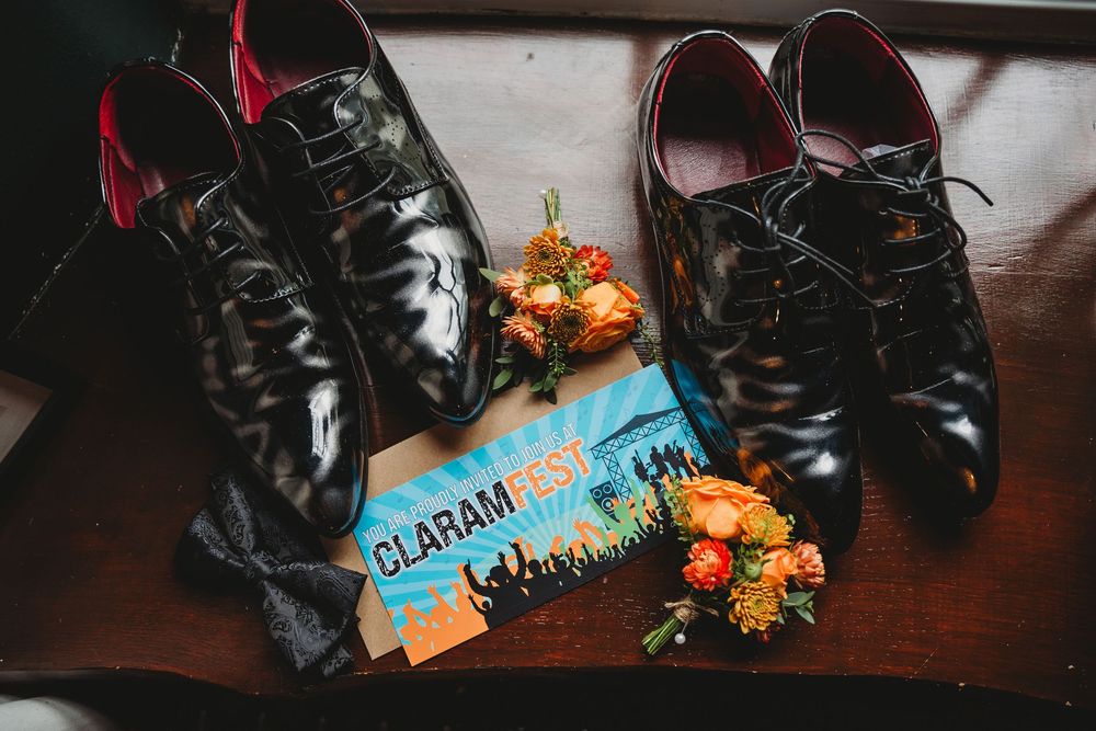 Two pairs of black dress shoes with orange floral boutonnieres and a Claram Fest ticket.