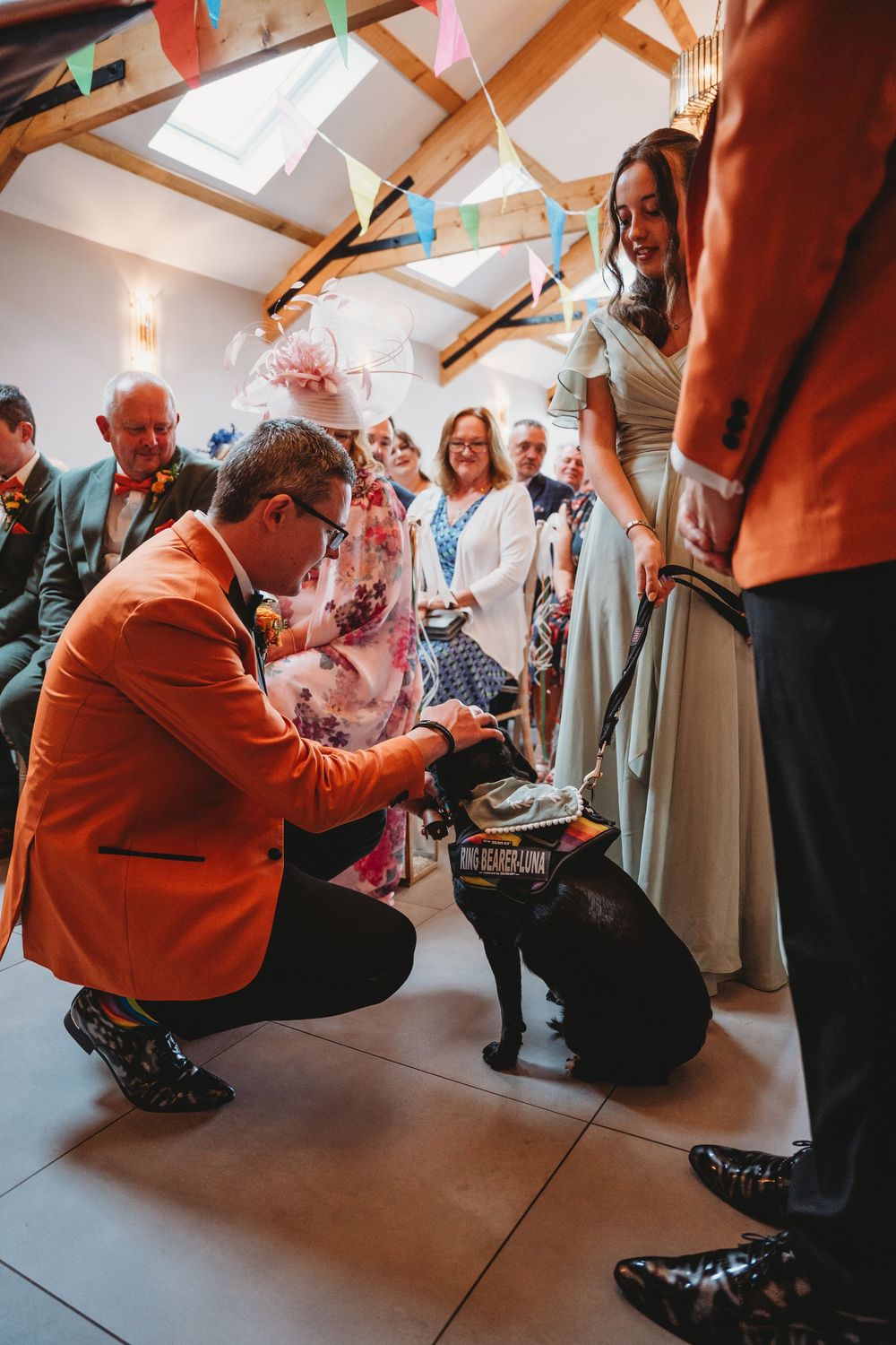 Group of people in formal attire gathering around someone in an orange jacket. Gellifawr Woodland Retreat
