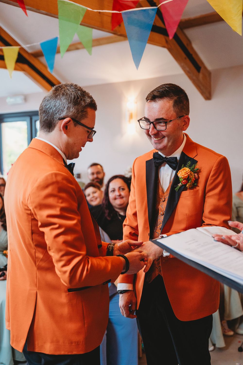 People in orange jackets standing under colorful bunting at an indoor celebration. Gellifawr Woodland Retreat