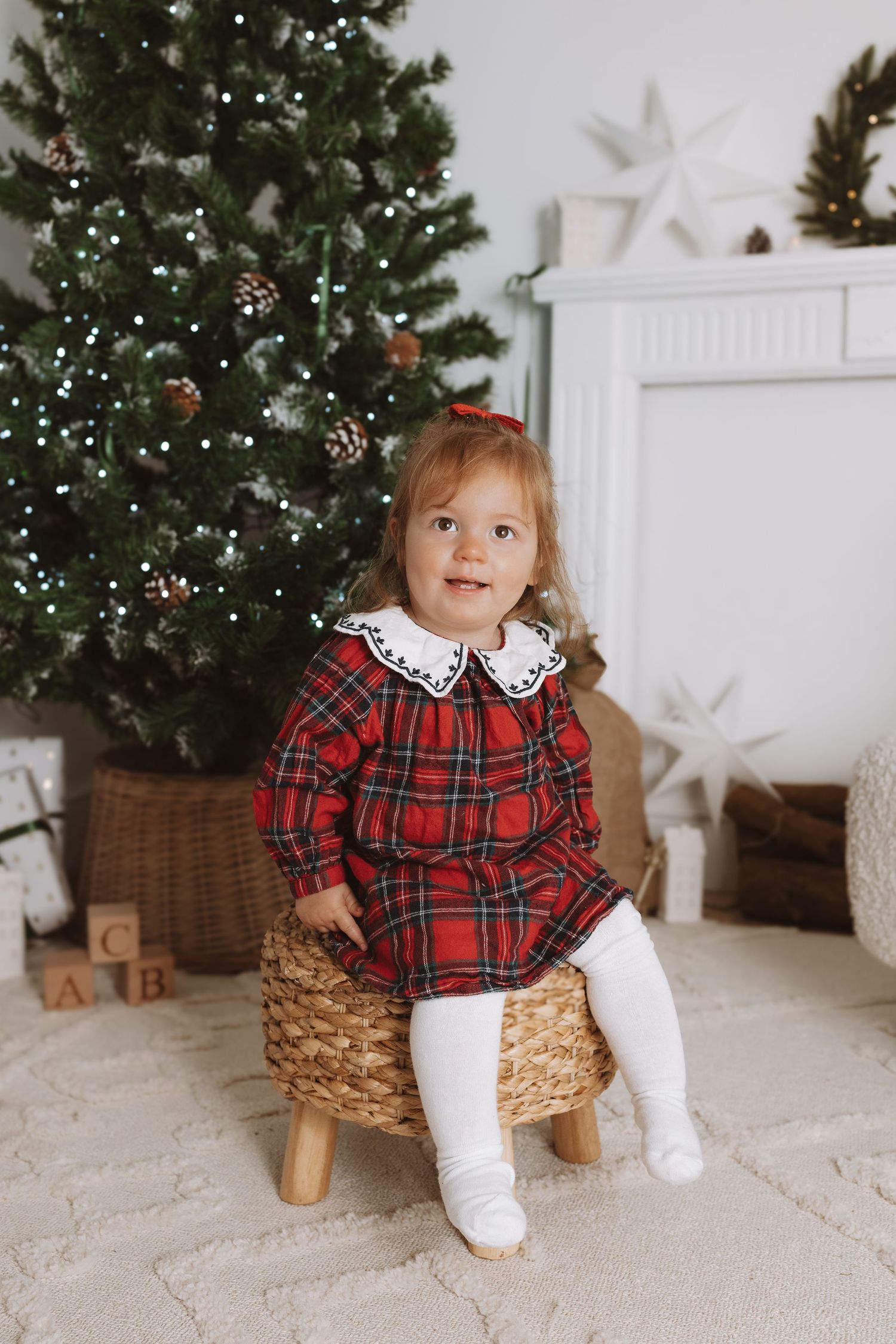 A child in a white top and brown pants poses playfully against a white backdrop decorated with star designs.