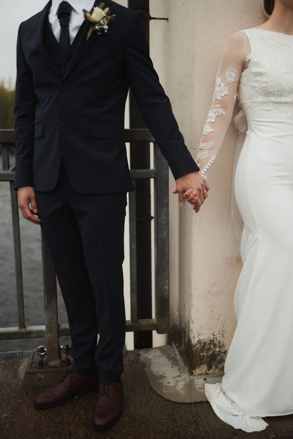 Wedding couple photographed from waist down holding hands in formal attire.