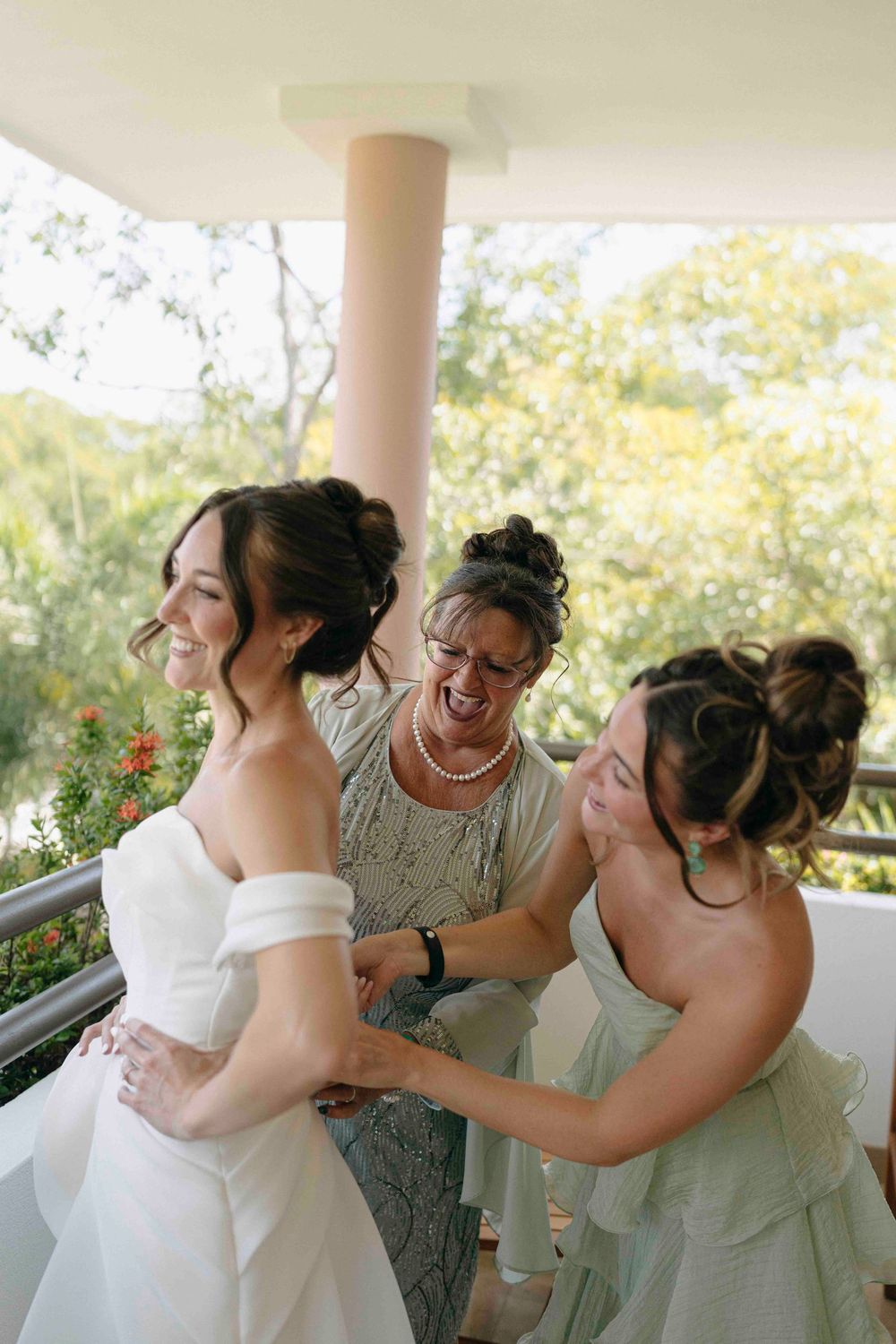 Joyful candid moments of mom and sister of the bride laughing and embracing during a wedding celebration on a balcony.
